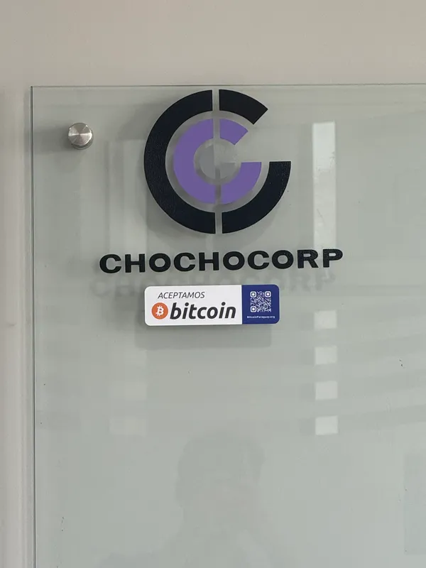 Placa da Chochocorp com o selo “Aceitamos Bitcoin”